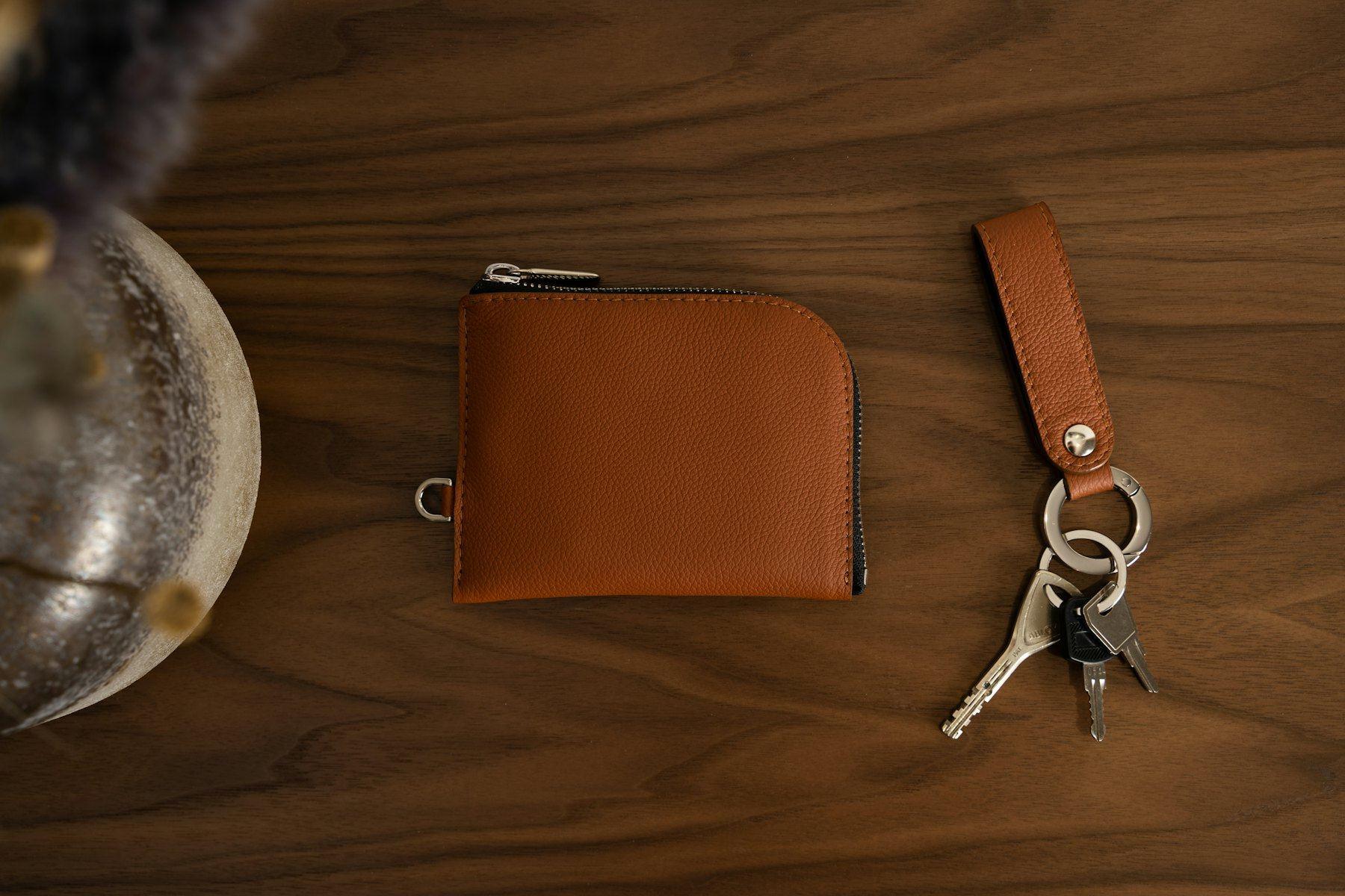 A leather wallet and keys on a walnut table