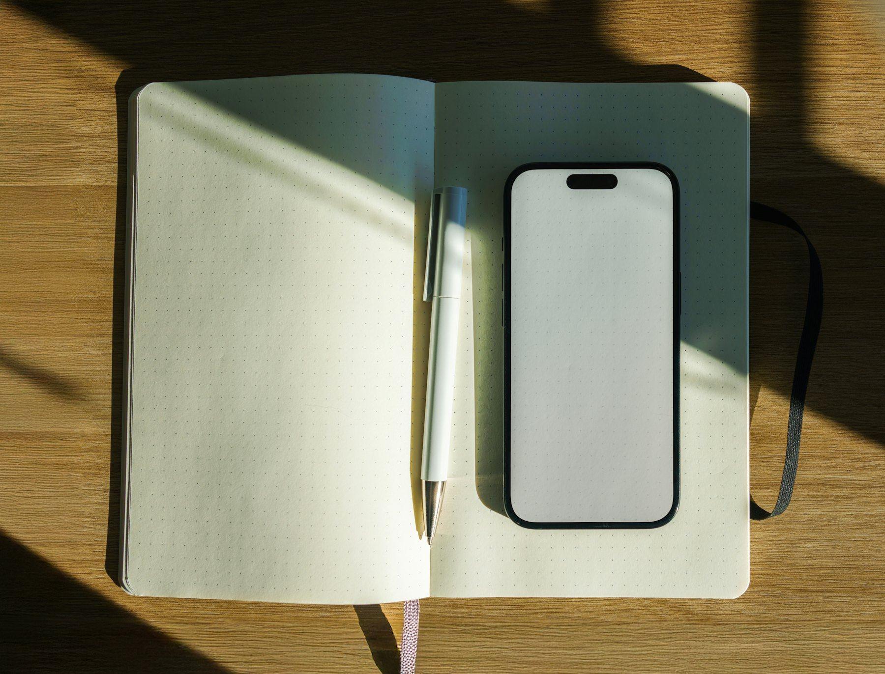 A notebook, pen and phone on a wooden table